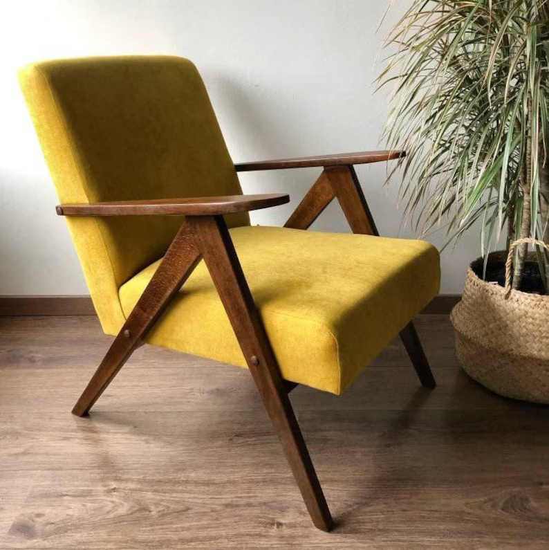 A mustard coloured chair with wooden legs in the ‘mid century modern’ style